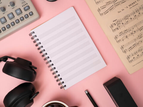 A music manuscript notebook, surrounded by classical sheet music, headphones and a synth.